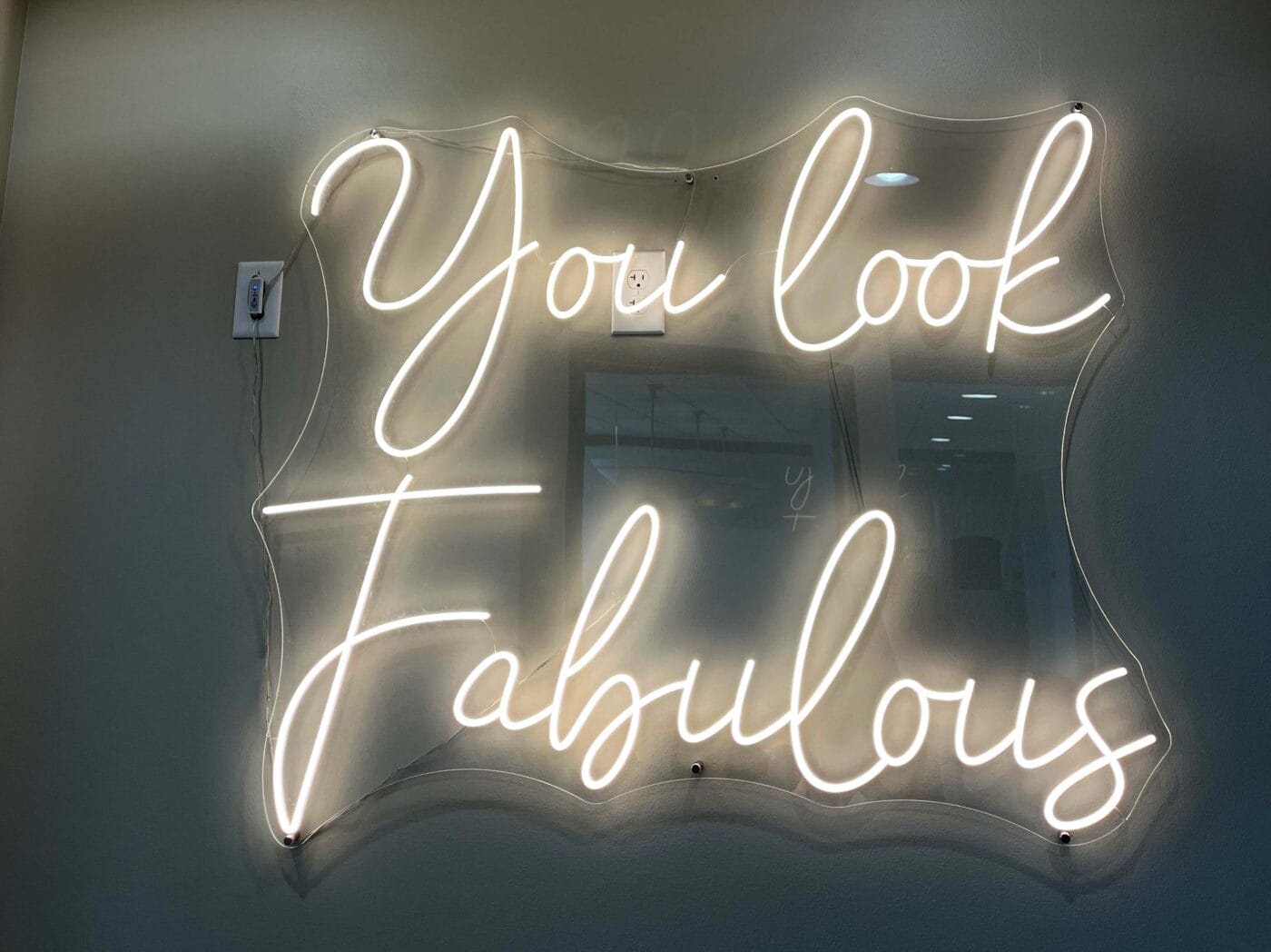 Neon sign on a wall displays the words “You look Fabulous” in cursive lettering, with a power outlet above the left corner—perfectly highlighting the need for reliable Electrical Service Upgrades to safely power vibrant décor.