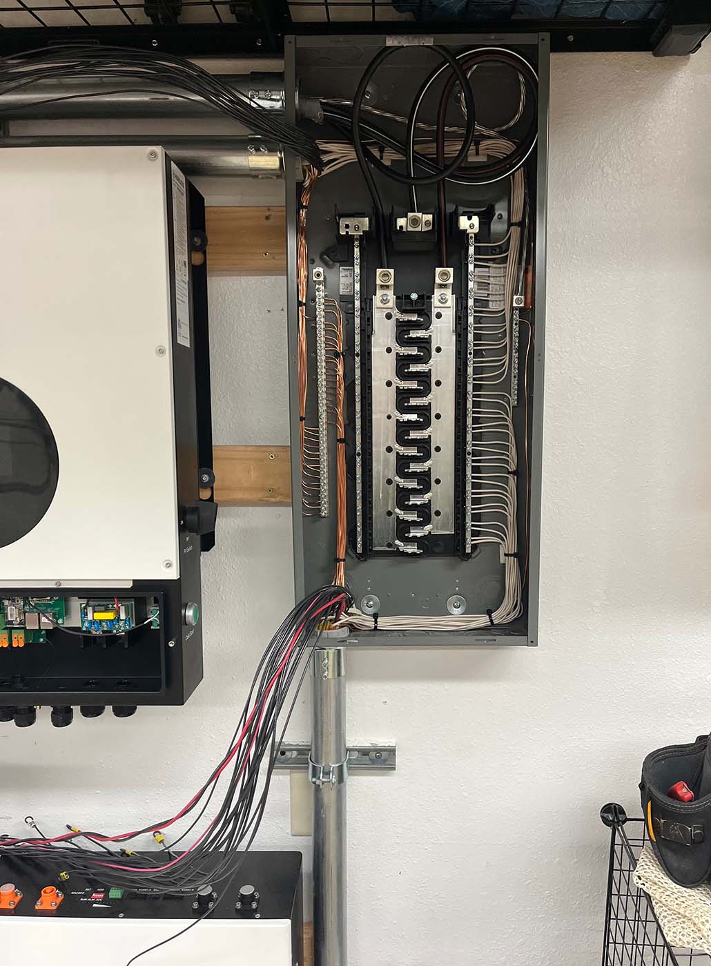 Open electrical panel with exposed wiring, showing organized circuit breakers, copper ground wires, and conduit entering from the bottom.